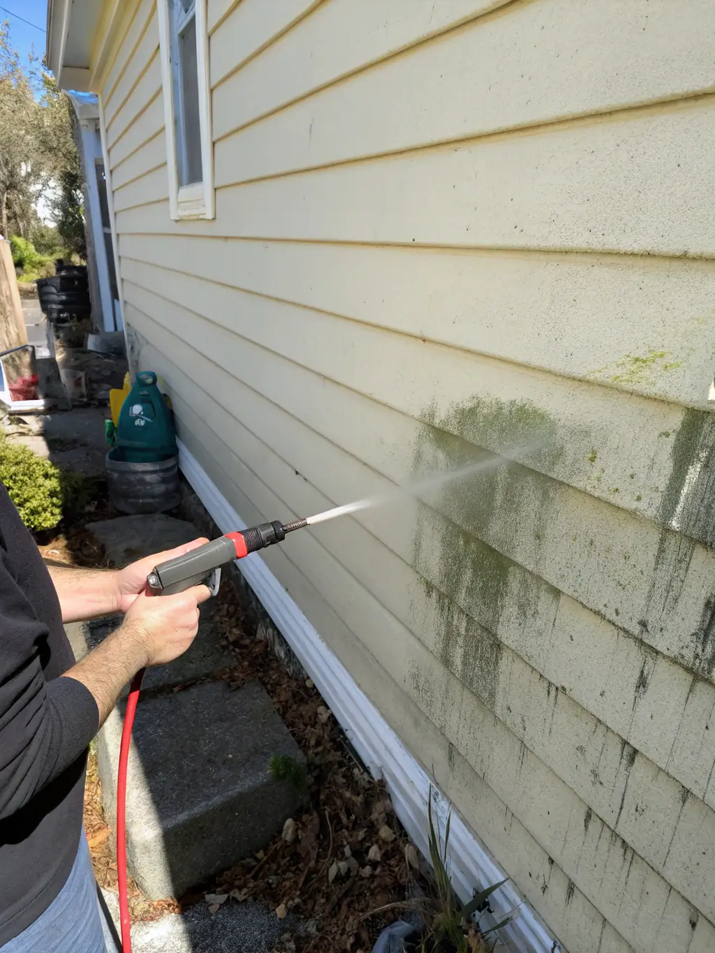 A clean, two-story house with light beige siding being pressure washed, showcasing the removal of dirt and grime, emphasizing the effectiveness of Premier Wave's house washing service.